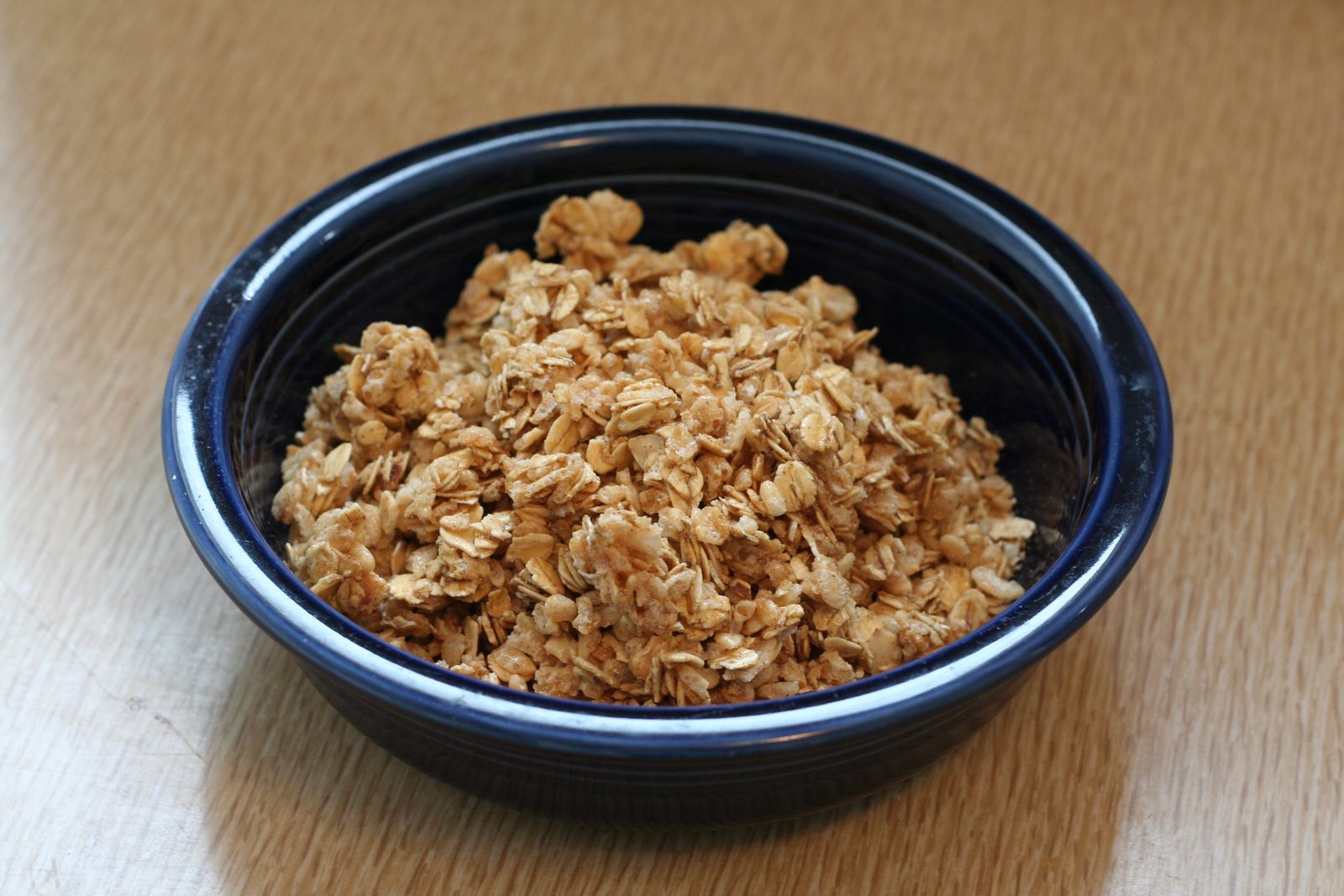 A dark blue bowl of granola clusters on a wooden table