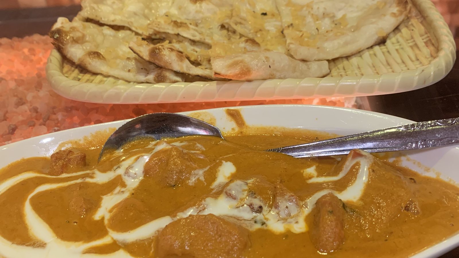 A basket of naan bread beside a plate of butter chicken curry with a spoon, at an Indian restaurant