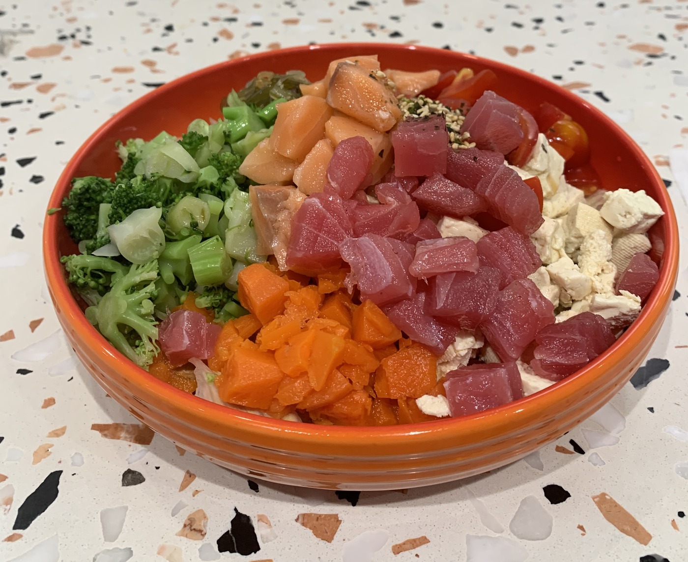 A poke bowl with salmon, tuna, broccoli, carrot and tofu, freshly assembled